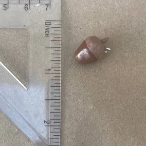 Detailed close-up view of a brown acorn charm pendant next to a ruler for size measurement