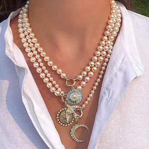 Détail d'un collier de perles multicouches avec pendentifs soleil, lune et oiseau sur chemise blanche