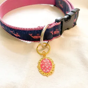 Adjustable pink and navy blue pet collar with whale pattern and gold oval charm pendant.