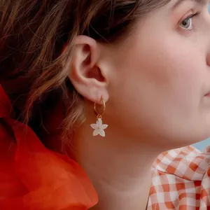 Elegant gold hoop earring with white flower pendant worn by model in soft lighting