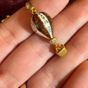 Gros plan d'un pendentif montgolfière doré avec motifs en émail et pierres claires