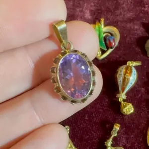 Détail d'un pendentif ovale en améthyste avec un cadre texturé doré tenu à la main