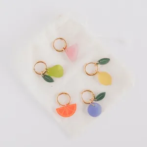 Detail of colorful fruit charms including lemon and orange on a white cloth bag.