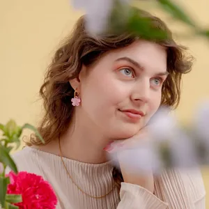 Close-up of a model wearing a delicate pink floral pendant earring with a gold hoop