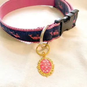 Close-up of ornate gold pendant with pink dots on a whale-patterned pet collar