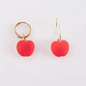 Detail view of red semi-transparent apple charms on gold stainless steel hoop earrings