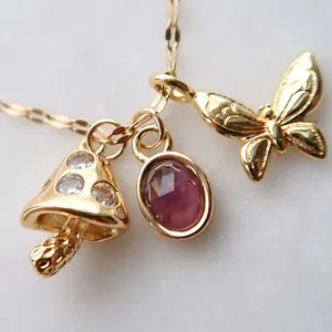 Nahaufnahme goldener Schmetterlings- und Pilzanhänger mit lila Edelstein an Kette