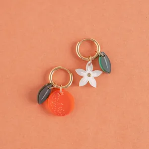 Close-up of asymmetrical fruit and flower charms on gold stainless steel hoop earrings