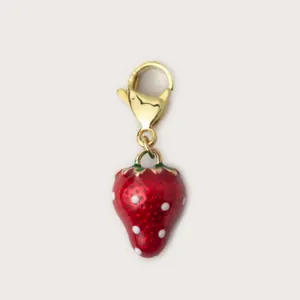 Dettaglio di un ciondolo a fragola rosso con punti bianchi e chiusura a moschettone oro.