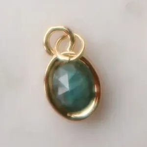 Detailaufnahme eines facettierten blaugrünen Zirkon-Anhängers mit goldener Edelstahlfassung.