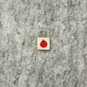 Minimalist handmade ceramic tomato pendant with gold stainless steel ring on stone surface.