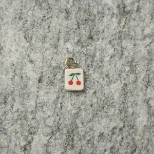 Macro detail of a square white pendant featuring a vibrant cherry design and gold ring.