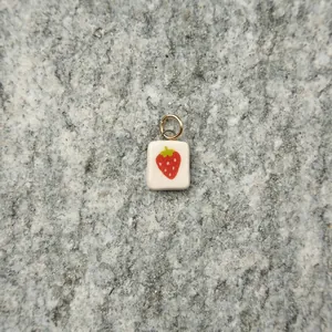 Macro detail of a cute strawberry charm pendant resting on a gray stone surface