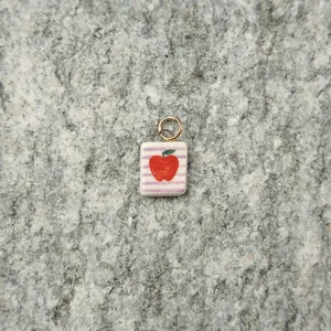 Close-up of a square ceramic pendant featuring a red apple design on a stone background.