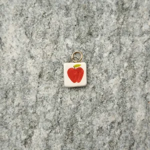 Close-up of a white square ceramic pendant featuring a hand-painted red apple design.