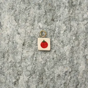 Close-up of a handmade square ceramic tomato pendant with a gold ring.