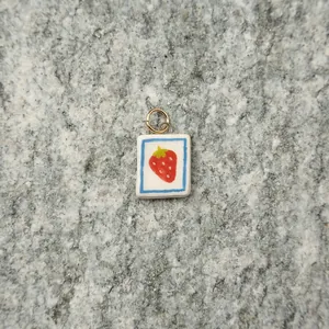 Close-up view of a minimalist white square ceramic strawberry pendant on stone texture