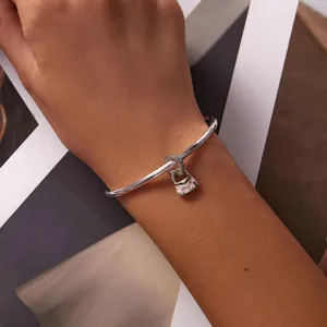 Détail en gros plan d'un jonc en acier titane avec un charm sac à main à cœurs roses