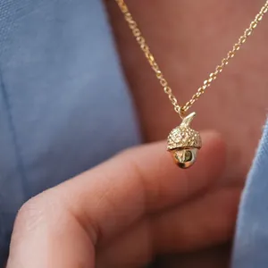 Close-up detail of a textured gold acorn pendant necklace on a delicate gold chain.
