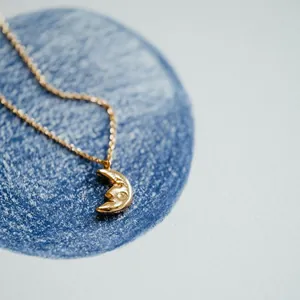 Detailed macro shot of a gold moon face pendant necklace on blue and white background