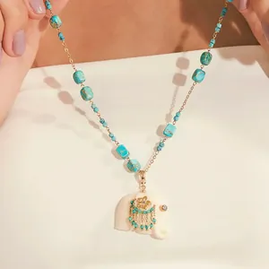 Close-up of white elephant pendant necklace with turquoise stone beads and gold floral detail
