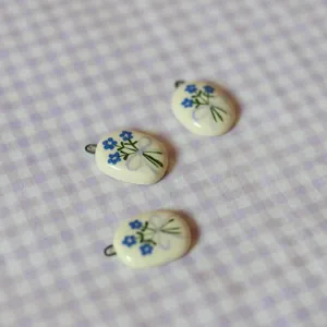 Macro detail of cream oval ceramic pendants featuring elegant blue flower and purple bow designs