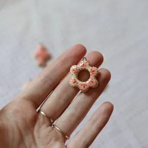 Detailed close-up of a small handmade pink floral ceramic-style pendant held in fingers