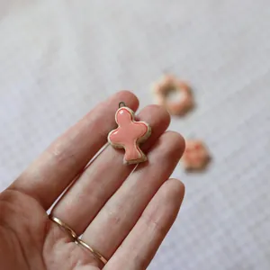 Detail shot of a pink cross pendant held between fingers showing its small size.