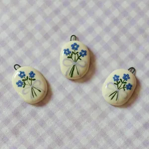 Macro view of oval ceramic jewelry pendants featuring hand-painted blue floral bouquets