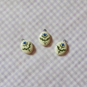 Detailed view of three oval ceramic pendants with blue floral designs on purple gingham background