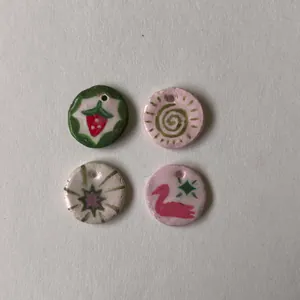Close-up of four colorful hand-painted DIY round charms with strawberry and swan motifs