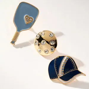 Detail view of sports-themed charms featuring a blue paddle, rhinestone ball, and baseball cap.