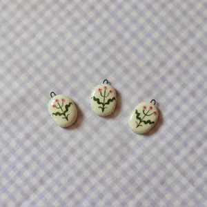 Close-up of handmade oval ceramic pendants with delicate floral design on gingham