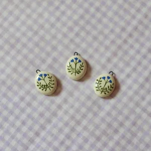 Close-up of oval ceramic pendants featuring hand-painted blue flowers and green leaves