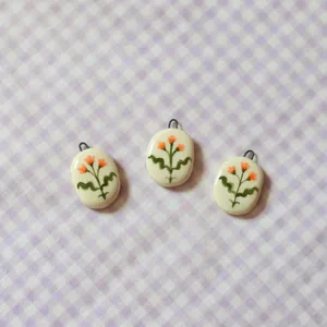 Detail view of three oval white pendants with hand-painted orange flowers on gingham