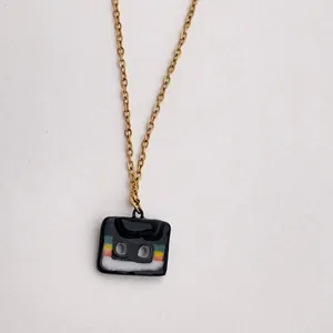 Gros plan d'un collier avec pendentif style cassette rétro et rayures colorées sur chaîne dorée