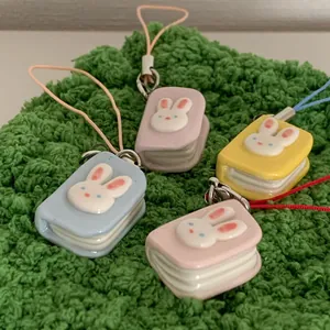 Detailed view of four colorful mini book charms with cute 3D rabbit designs on green fabric.