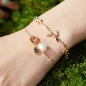 Detailed view of gold-tone bracelets with pearl and rabbit charms on a mossy background