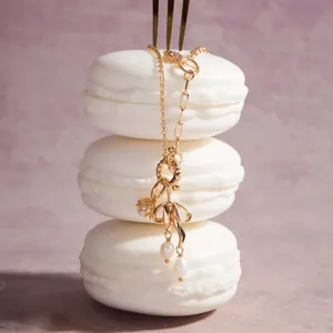 Detail view of a gold stainless steel necklace with pearl bow charms on white macarons.
