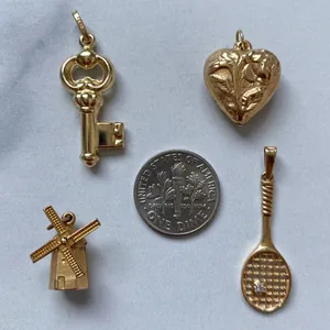Detailed macro of gold heart windmill key and tennis racket pendants with a dime for scale