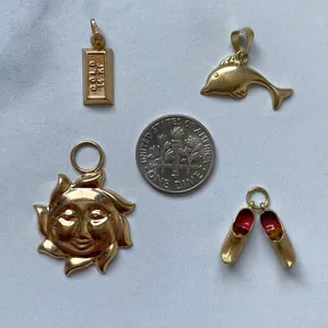 Detailed view of gold-toned pendants including a sun face and dolphin near a US dime coin.