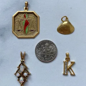 Detailed view of gold pendants featuring Libra scale, seashell and initial K pendant