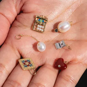 A variety of colorful enamel and pearl charms held in a palm for size perspective.