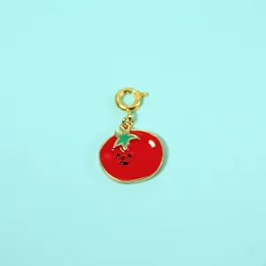 Macro detail of cute cartoon tomato pendant featuring red enamel and a gold-plated clasp