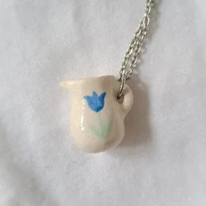 Close-up of ceramic-style pitcher pendant with blue tulip detail on chain