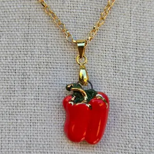 Nahaufnahme eines leuchtend roten Emaille-Paprika-Anhängers an einer feinen Goldkette