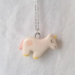 Detailed close-up of a minimalist pink unicorn enamel pendant on a silver stainless steel chain