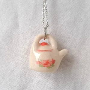 Detailed macro shot of a miniature ceramic teapot pendant with beautiful red floral patterns