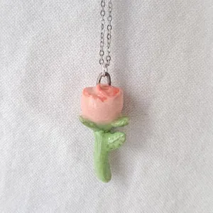 Macro detail of a pink rose pendant with green leaves and drip oil enamel finish.