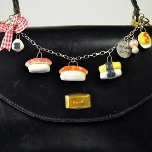 Détail de la chaîne à breloques sushi en acier inoxydable avec nœud et perles.